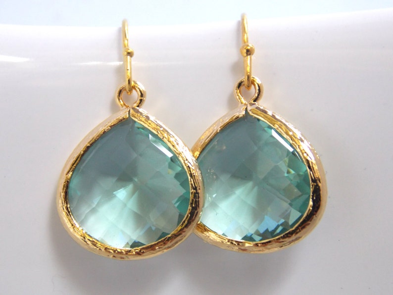 May include: A pair of gold teardrop earrings with light blue crystal stones.