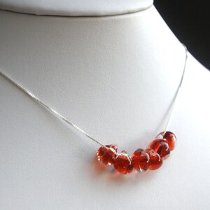 May include: A silver chain necklace with a row of red glass beads.