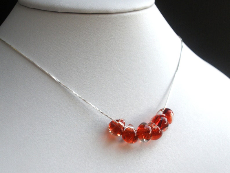 May include: A silver chain necklace with a row of red glass beads.
