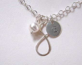 Puede incluir: Collar de plata con un dije de perla, un dije de símbolo de infinito y un dije redondo con la letra "E" grabada.