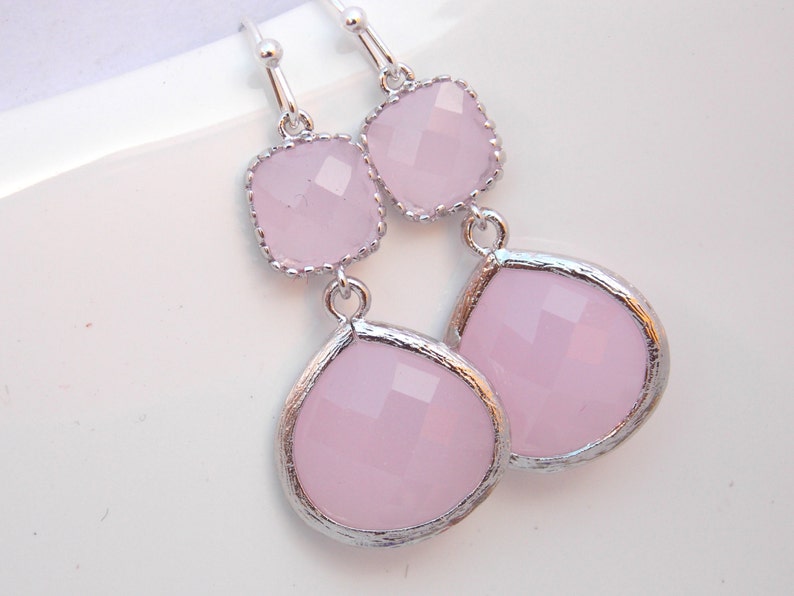 May include: A pair of silver dangle earrings with pink faceted glass stones. The earrings have a square stone at the top and a teardrop-shaped stone at the bottom.