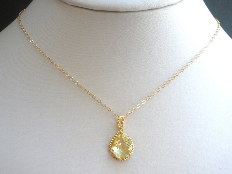 May include: A gold chain necklace with a teardrop-shaped pendant featuring a yellow gemstone.