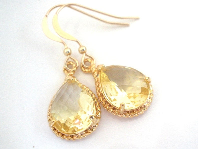 May include: Gold teardrop earrings with a yellow gemstone. The earrings have a twisted rope design around the gemstone.