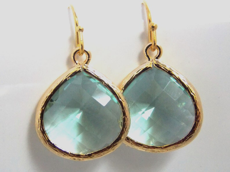 May include: A pair of gold teardrop earrings with light blue crystal stones.