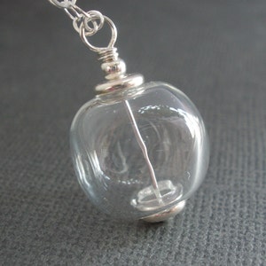 May include: A silver chain necklace with a clear glass orb pendant. The orb has a silver cap on the top and bottom.