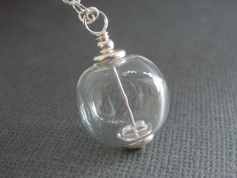 May include: A silver chain necklace with a clear glass orb pendant. The orb has a silver cap on the top and bottom.
