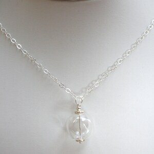 May include: A silver chain necklace with a clear glass pendant. The pendant is round and has a small silver cap on top.