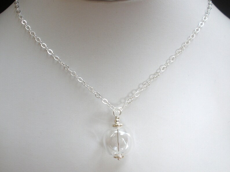 May include: A silver chain necklace with a clear glass pendant. The pendant is round and has a small silver cap on top.