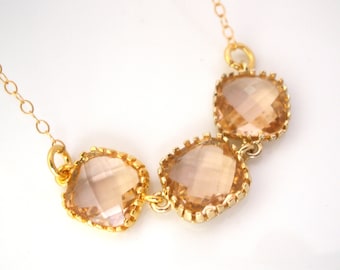 May include: A gold chain necklace with three large, faceted, light brown crystal stones. The stones are set in gold bezels and have a square shape.