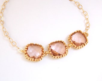 May include: A delicate gold chain bracelet with three square-shaped pink crystals. The crystals are set in gold bezels and have a faceted design.