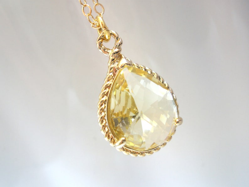 May include: A gold necklace with a teardrop-shaped yellow crystal pendant.
