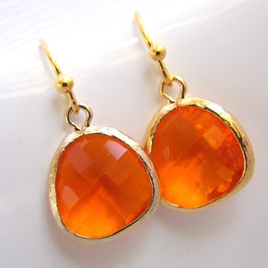 Puede incluir: Un par de pendientes colgantes de oro con piedras de cristal facetadas de color naranja. Los pendientes tienen un diseño simple y elegante.