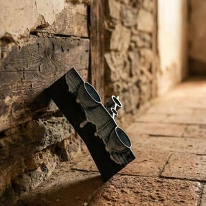 Puede incluir: Un bloque rectangular de cerámica negra que presenta dos cuencos circulares empotrados en su superficie frontal. El esmalte negro está acentuado con patrones de goteo blancos que corren verticalmente por la superficie oscura, creando un contraste.