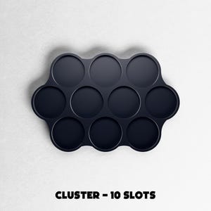 May include: A dark navy blue cluster tray with ten circular slots. The tray is on a white background. The text "CLUSTER - 10 SLOTS" is printed in black at the bottom of the image.