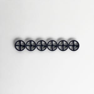Pode incluir: Seis objetos circulares azuis escuros com um design em forma de cruz no centro, dispostos horizontalmente sobre um fundo branco. Os objetos t&ecirc;m uma apar&ecirc;ncia semelhante a rodas, com um cubo central e raios.