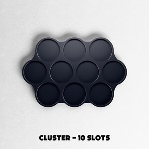 May include: A dark navy blue cluster tray with ten circular slots. The tray has a unique, curved shape and is set against a white background. The text "CLUSTER - 10 SLOTS" is printed in bold, black letters at the bottom.