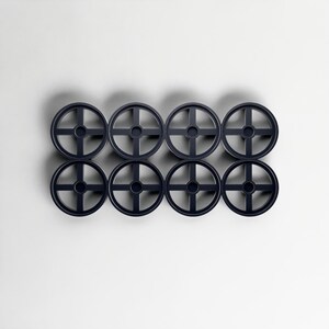 May include: Eight dark blue, circular objects with a cross-shaped design inside, arranged in two rows of four. The objects are evenly spaced against a white background, creating a symmetrical pattern. The design is simple and modern.