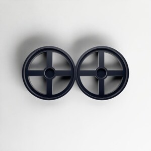 Pode incluir: Dois objetos circulares azul marinho com um design em forma de cruz no interior. Os objetos s&atilde;o sim&eacute;tricos e parecem ser feitos de um material s&oacute;lido. O fundo &eacute; branco liso.