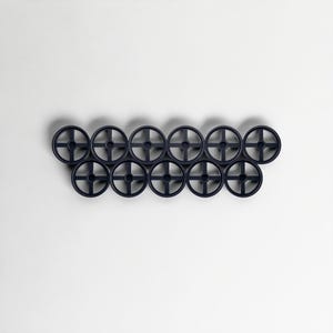 Pode incluir: Uma cole&ccedil;&atilde;o de doze objetos decorativos azuis marinhos em forma de roda, dispostos em duas filas de seis. Cada roda tem um design em forma de cruz no centro. Os objetos est&atilde;o sobre um fundo branco liso.