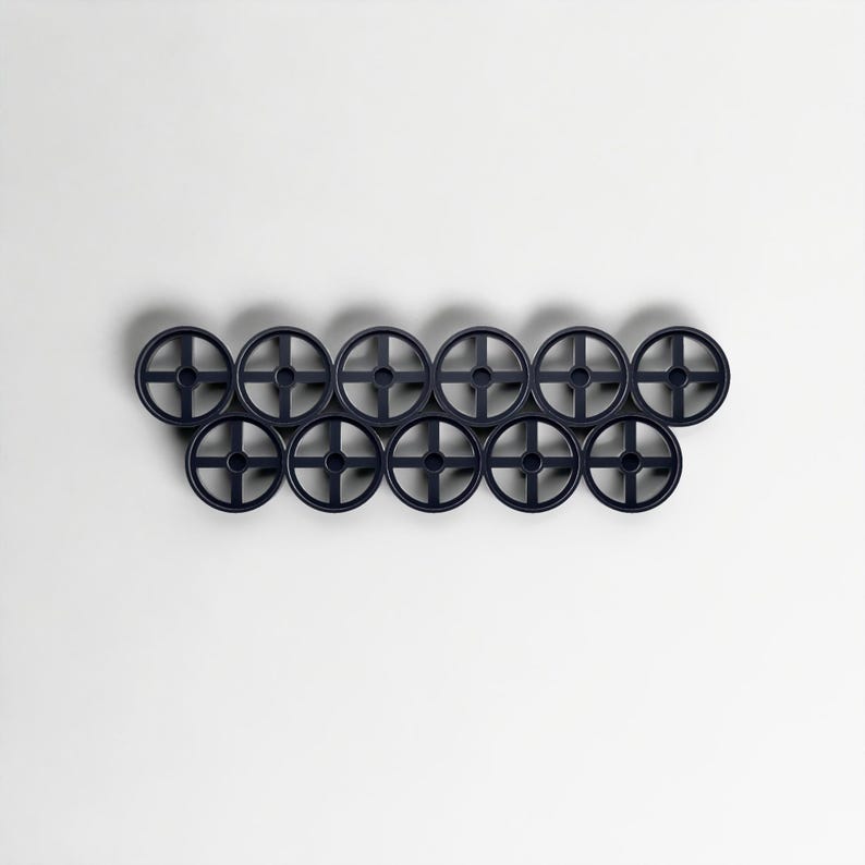 Pode incluir: Uma cole&ccedil;&atilde;o de doze objetos decorativos azuis marinhos em forma de roda, dispostos em duas filas de seis. Cada roda tem um design em forma de cruz no centro. Os objetos est&atilde;o sobre um fundo branco liso.