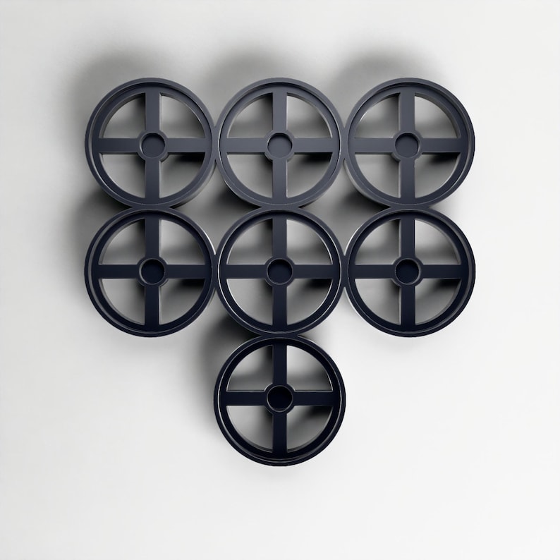 May include: Seven dark grey, circular objects with a cross-shaped design are arranged in a pattern against a white background. The objects appear to be made of a solid material and have a minimalist aesthetic.