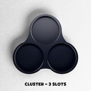 May include: A dark navy blue cluster with three circular slots. The object is made of a smooth material and is set against a white background. The text "CLUSTER - 3 SLOTS" is displayed at the bottom of the image.