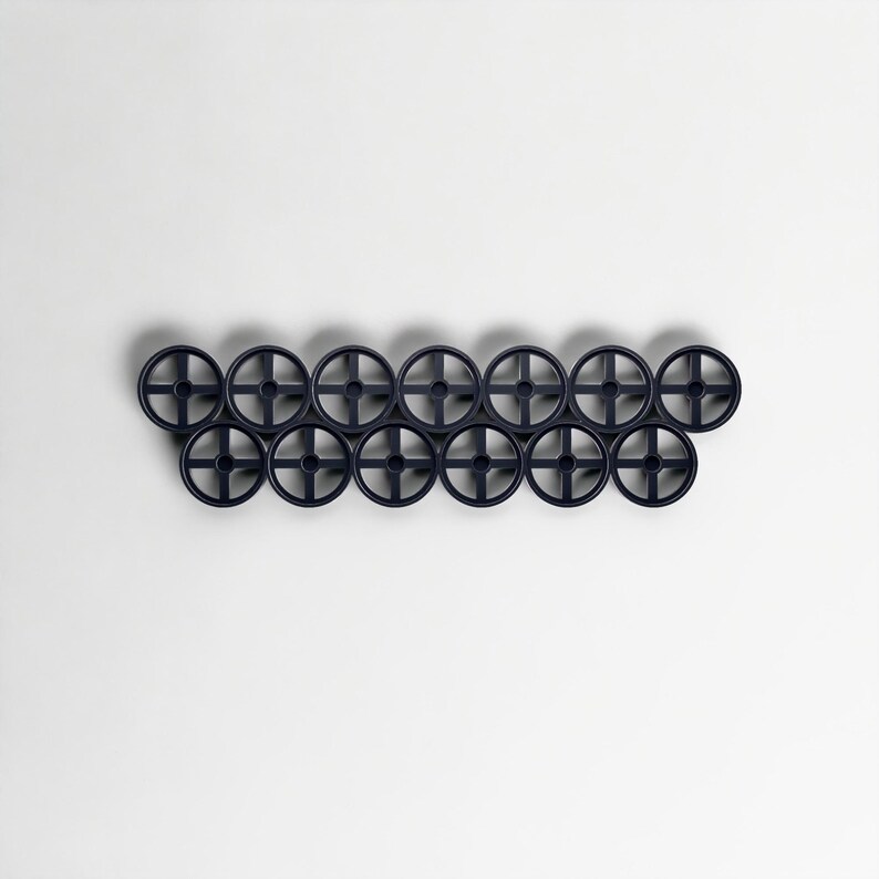 Pode incluir: Um cabide de parede azul marinho escuro com uma s&eacute;rie de ganchos circulares em forma de roda. Os ganchos est&atilde;o dispostos horizontalmente, criando um design moderno e minimalista. O cabide &eacute; feito de um material s&oacute;lido e est&aacute; sobre um fundo branco liso.