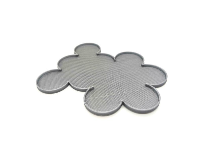 May include: A gray, cloud-shaped trivet with a textured surface. The trivet has a series of rounded lobes, resembling a stylized flower or cloud. The trivet is made of a solid material and is designed to protect surfaces from heat.
