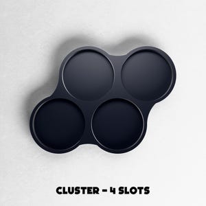 May include: A dark navy blue cluster with four circular slots. The slots are arranged in a unique pattern, with three slots clustered together and one separate. The text "CLUSTER - 4 SLOTS" is displayed in bold, black font at the bottom of the image.