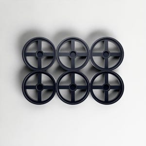 May include: Six dark navy blue, circular objects with a cross-shaped design, arranged in two rows of three. Each object has a central hole. The objects are set against a plain white background, creating a minimalist aesthetic.