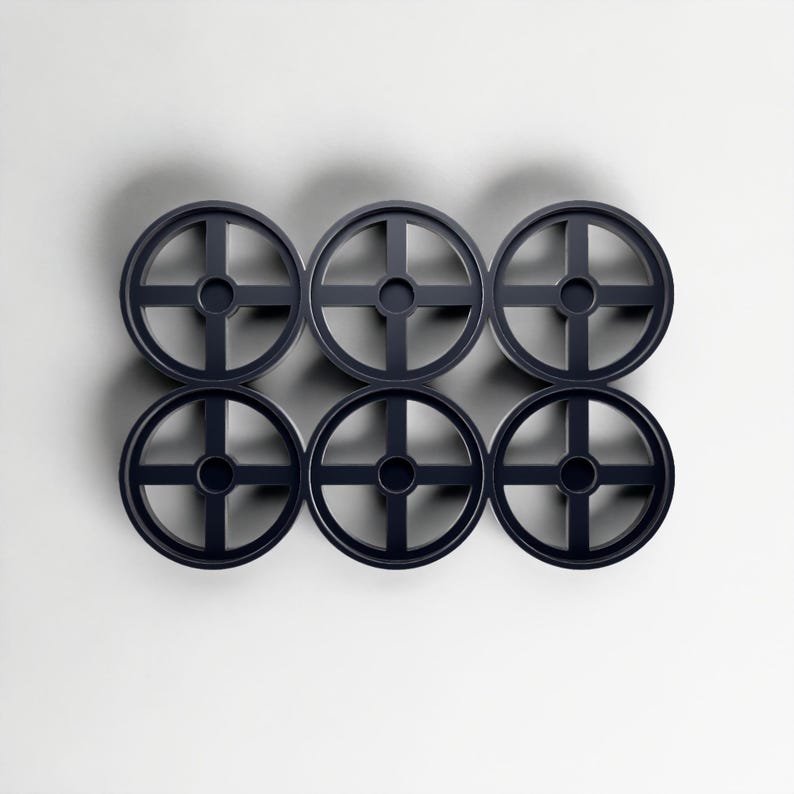 May include: Six dark navy blue, circular objects with a cross-shaped design, arranged in two rows of three. Each object has a central hole. The objects are set against a plain white background, creating a minimalist aesthetic.