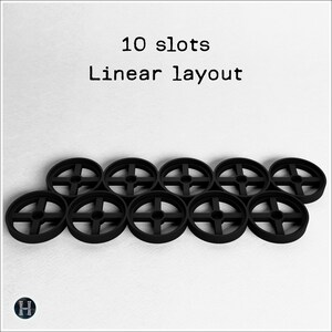 Pode incluir: Dez objetos circulares pretos com um design em forma de cruz s&atilde;o dispostos em um layout linear. O texto "10 slots Linear layout" est&aacute; acima dos objetos. Um logotipo est&aacute; no canto inferior esquerdo.