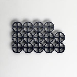May include: Fifteen dark grey circular objects with a cross-shaped design in the centre, arranged in a grid against a white background. The objects are evenly spaced and appear to be made of plastic. Each object has a diameter of approximately 5 cm.