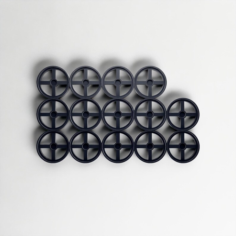 May include: Fifteen dark grey circular objects with a cross-shaped design in the centre, arranged in a grid against a white background. The objects are evenly spaced and appear to be made of plastic. Each object has a diameter of approximately 5 cm.