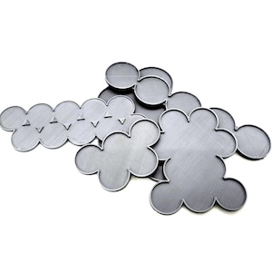 May include: A collection of gray, cloud-shaped metal coasters. The coasters have a textured surface and are arranged on a white background. Some coasters have a series of small, triangular cutouts along the edge.