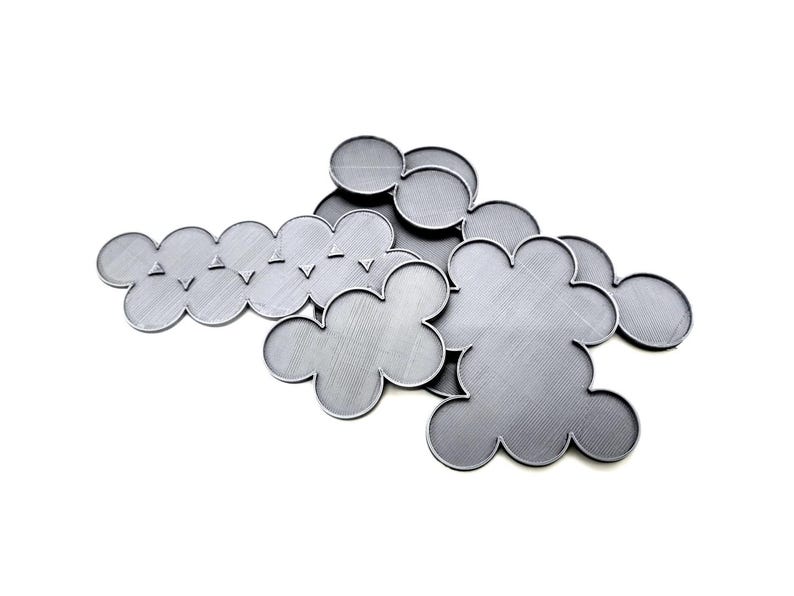 May include: A collection of gray, cloud-shaped metal coasters. The coasters have a textured surface and are arranged on a white background. Some coasters have a series of small, triangular cutouts along the edge.
