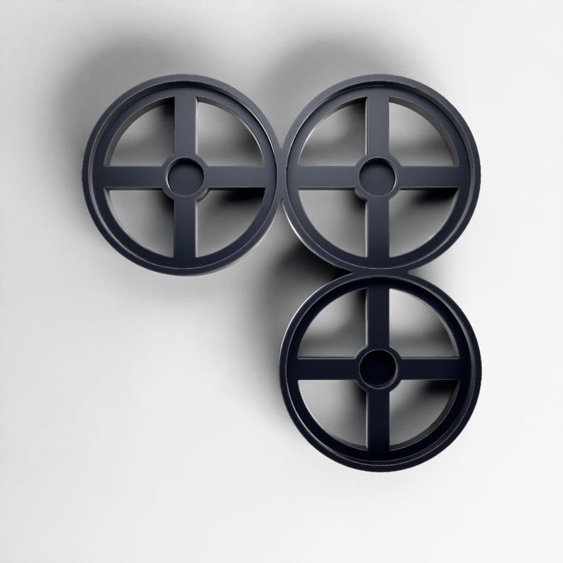 May include: Three dark grey, circular objects with a cross-shaped design, arranged in a cluster. The objects have a wheel-like appearance, with a central hub and spokes. The background is a plain white surface.