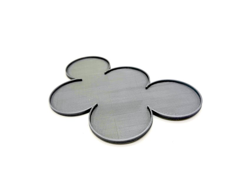 May include: A dark gray, four-leaf clover-shaped trivet with a textured surface and a raised edge. The trivet is made of a durable material and is designed to protect surfaces from heat.