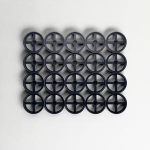 May include: Twenty-four dark blue circular objects, each with a cross-shaped design, arranged in a grid against a white backdrop. The objects are evenly spaced. They appear to be made of plastic. The objects are approximately 10 cm in diameter.