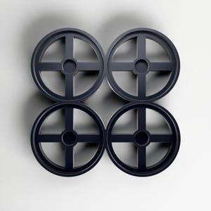 May include: Four dark grey, circular objects with a cross-shaped design inside, arranged in a square pattern. Each object has a central circular hole. The objects are set against a white background.