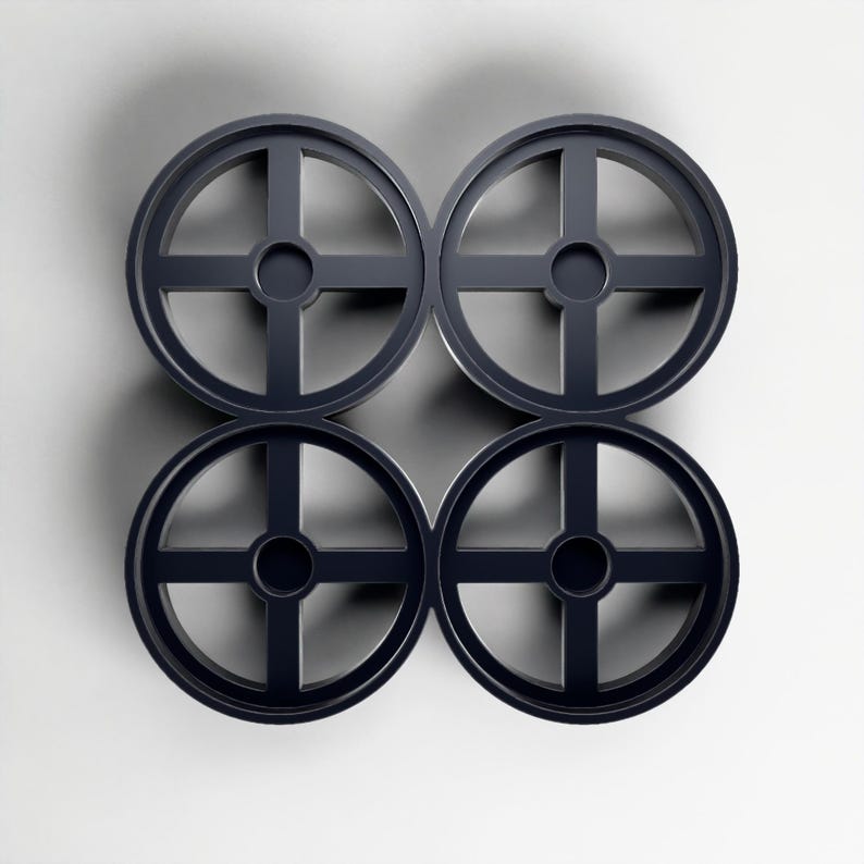 May include: Four dark grey, circular objects with a cross-shaped design inside, arranged in a square pattern. Each object has a central circular hole. The objects are set against a white background.
