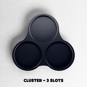 May include: A dark navy blue cluster with three circular slots. The object is made of a smooth material and is set against a white background. The text "CLUSTER - 3 SLOTS" is displayed at the bottom of the image.