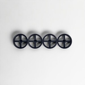 Pode incluir: Quatro ganchos de parede circulares azul marinho dispostos horizontalmente. Cada gancho apresenta um design em forma de cruz dentro do c&iacute;rculo, criando uma apar&ecirc;ncia de roda. Os ganchos est&atilde;o sobre um fundo branco liso, projetando sombras sutis.