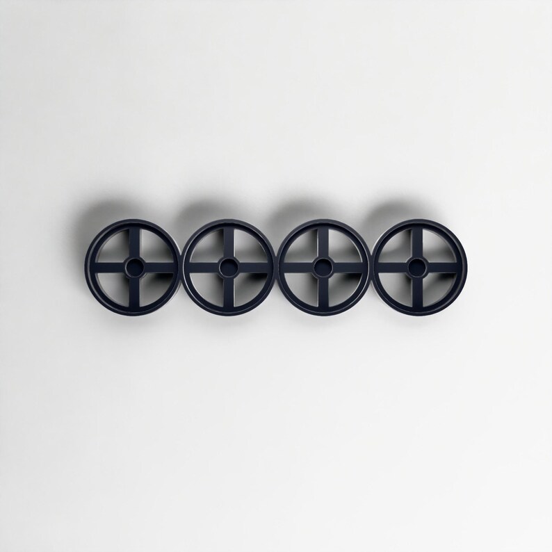 Pode incluir: Quatro ganchos de parede circulares azul marinho dispostos horizontalmente. Cada gancho apresenta um design em forma de cruz dentro do c&iacute;rculo, criando uma apar&ecirc;ncia de roda. Os ganchos est&atilde;o sobre um fundo branco liso, projetando sombras sutis.