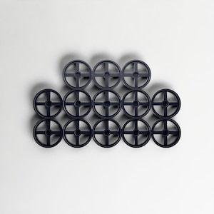 May include: Twelve dark grey plastic wheels with a cross-shaped design are arranged in a grid pattern. The wheels are evenly spaced against a white background. These wheels are likely for a toy or model.