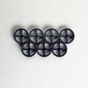Pode incluir: Uma cole&ccedil;&atilde;o de sete objetos circulares azuis escuros, semelhantes a rodas, dispostos em um grupo. Cada roda tem um orif&iacute;cio central e um design em forma de cruz. Os objetos est&atilde;o sobre um fundo branco liso.
