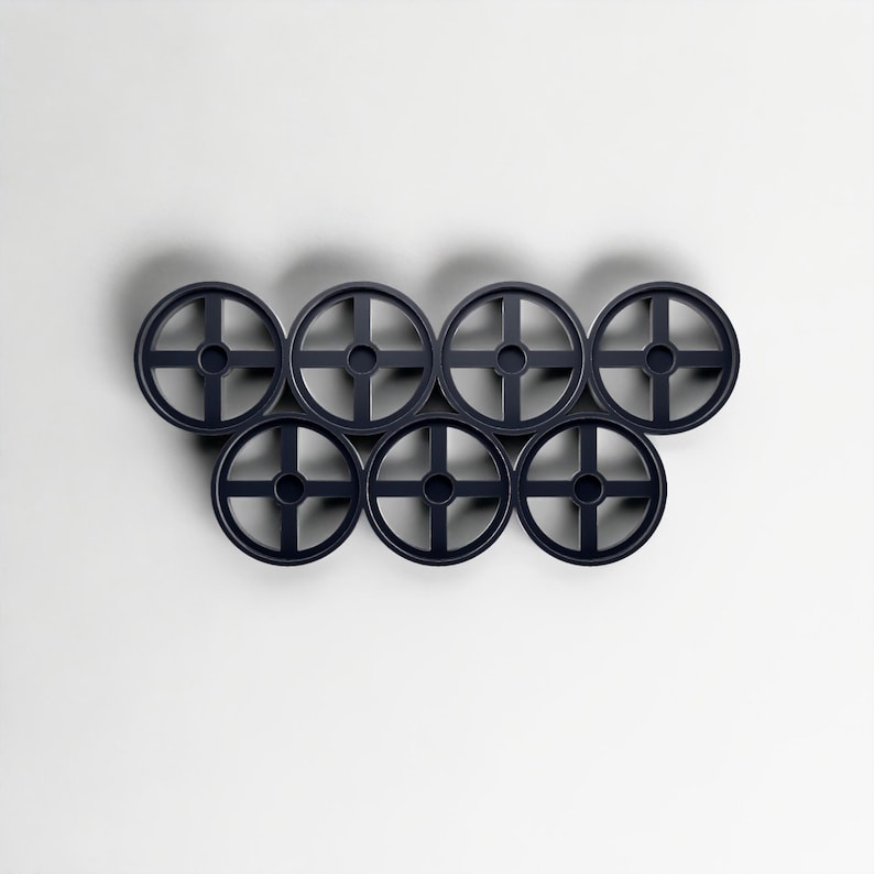Pode incluir: Uma cole&ccedil;&atilde;o de sete objetos circulares azuis escuros, semelhantes a rodas, dispostos em um grupo. Cada roda tem um orif&iacute;cio central e um design em forma de cruz. Os objetos est&atilde;o sobre um fundo branco liso.
