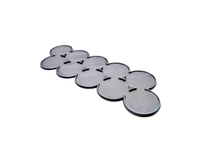 May include: A gray, flower-shaped object with a textured surface and small, triangular accents. The object is made of a solid material and is set against a white background. The design is modern and minimalist.