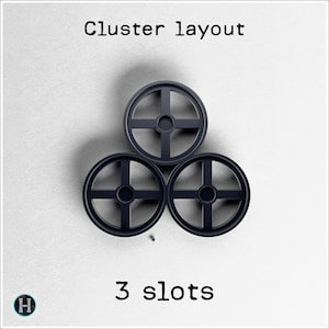 May include: Three dark gray circular objects with a cross-shaped design, arranged in a cluster layout. The text "Cluster layout" is at the top, and "3 slots" is at the bottom. A small logo is in the lower left corner.