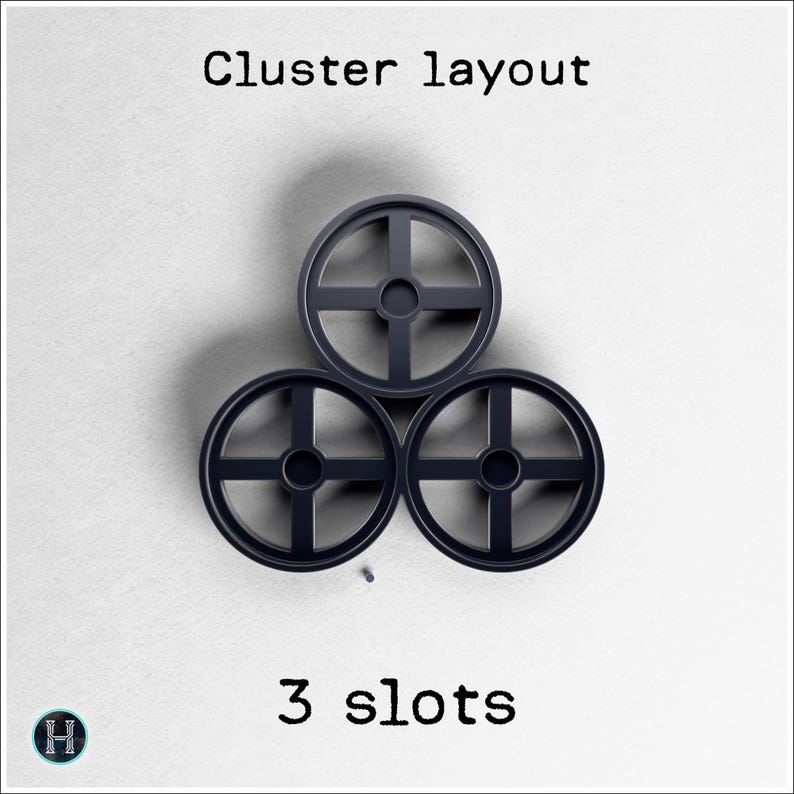 May include: Three dark gray circular objects with a cross-shaped design, arranged in a cluster layout. The text "Cluster layout" is at the top, and "3 slots" is at the bottom. A small logo is in the lower left corner.
